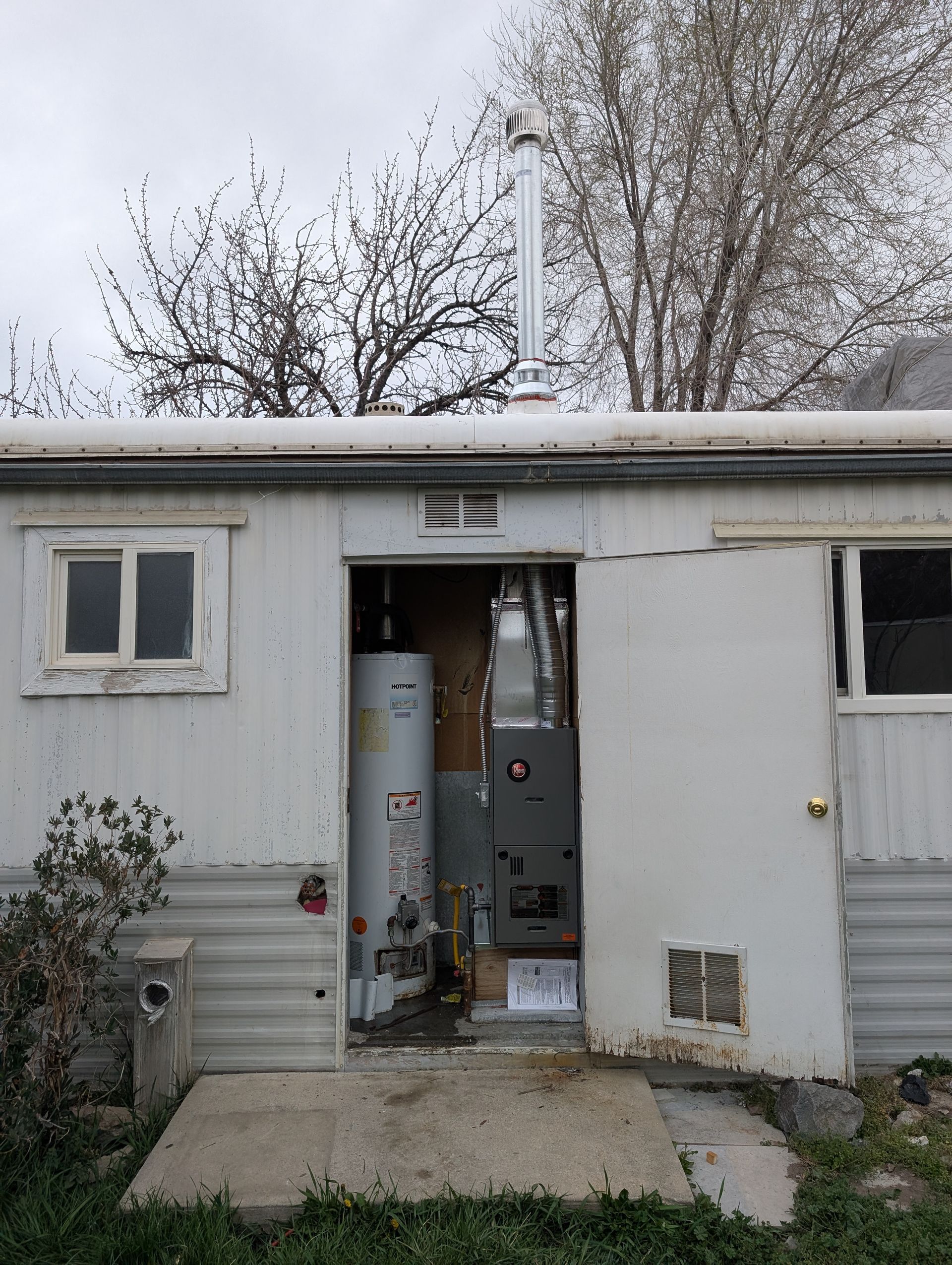 Open white utility shed with equipment inside, snow on the roof, and bare trees in the background