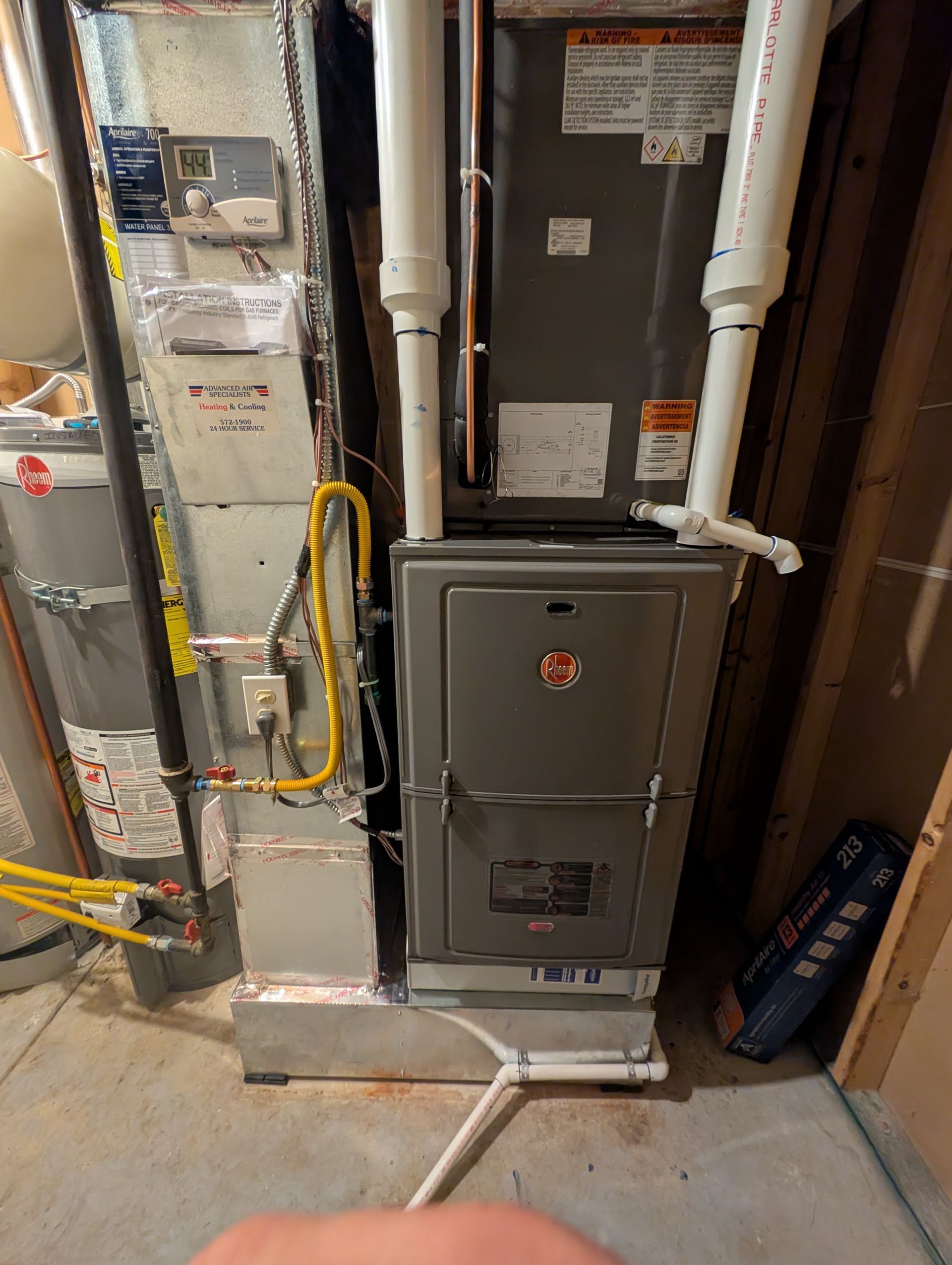 Furnace and utility cabinets in a basement with exposed pipes and a concrete floor.