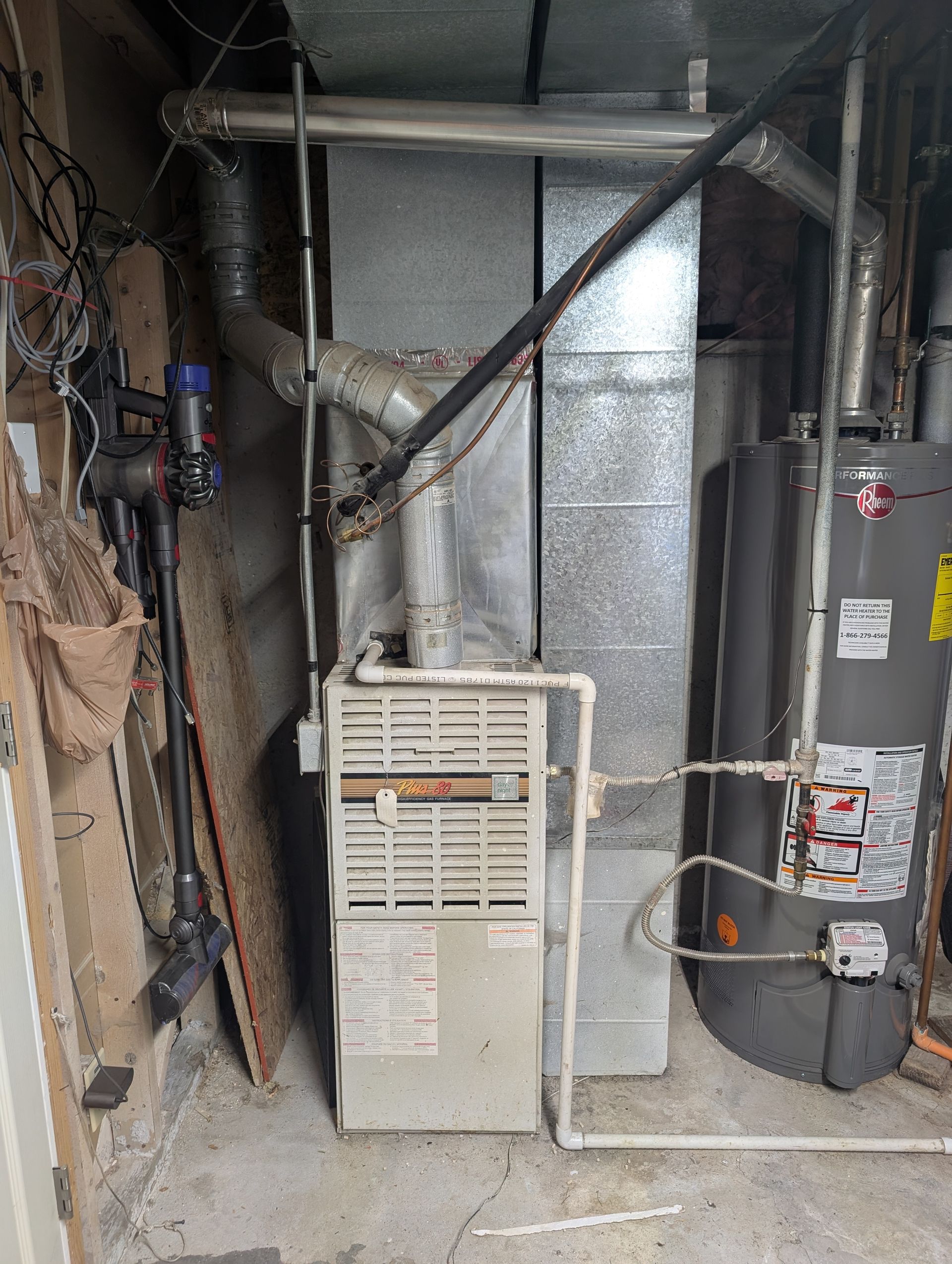 Utility room with furnace, water heater, exposed ductwork, and pipes against a concrete wall