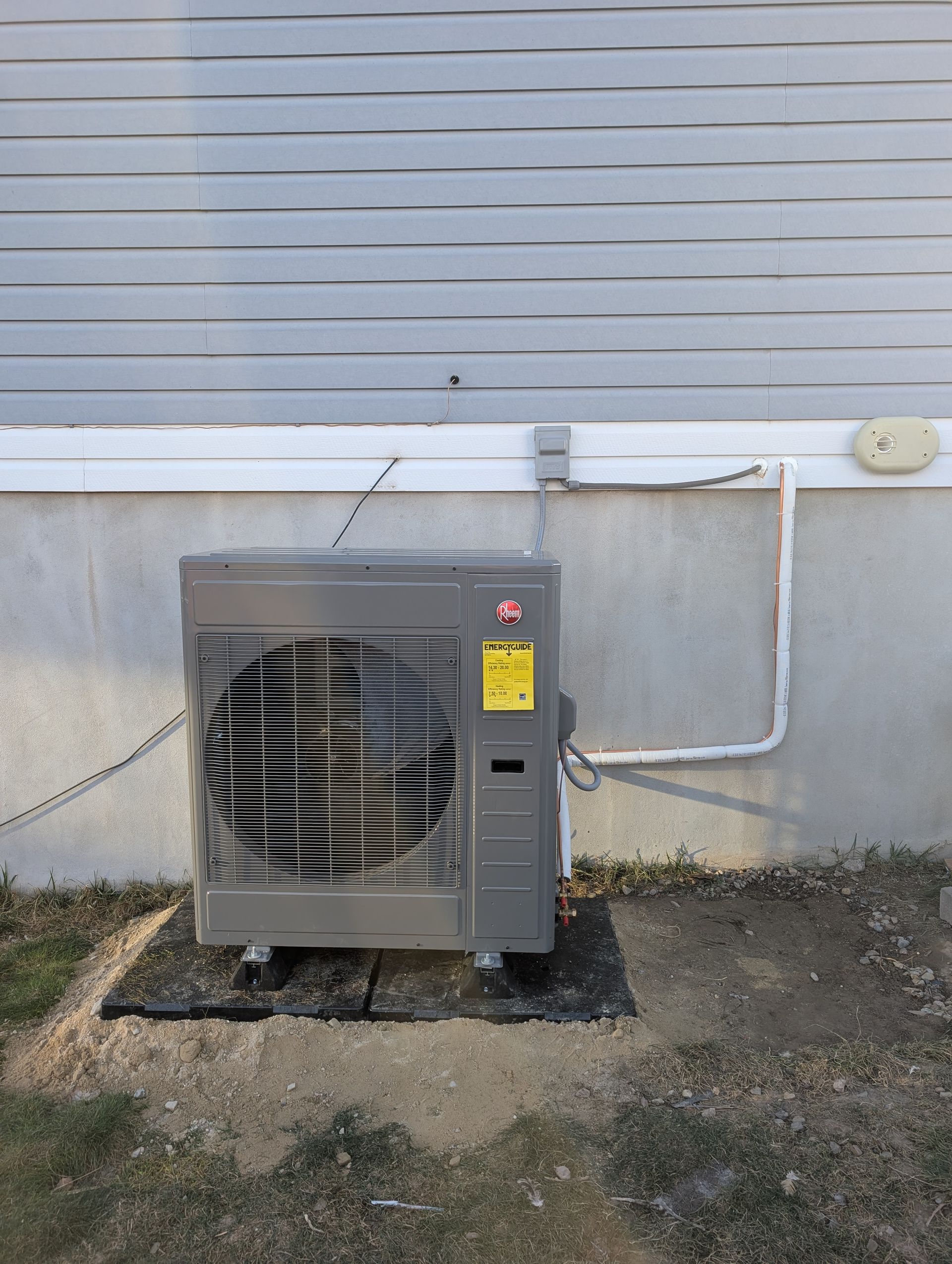 Outdoor HVAC unit beside a house wall with gray siding and a concrete pad