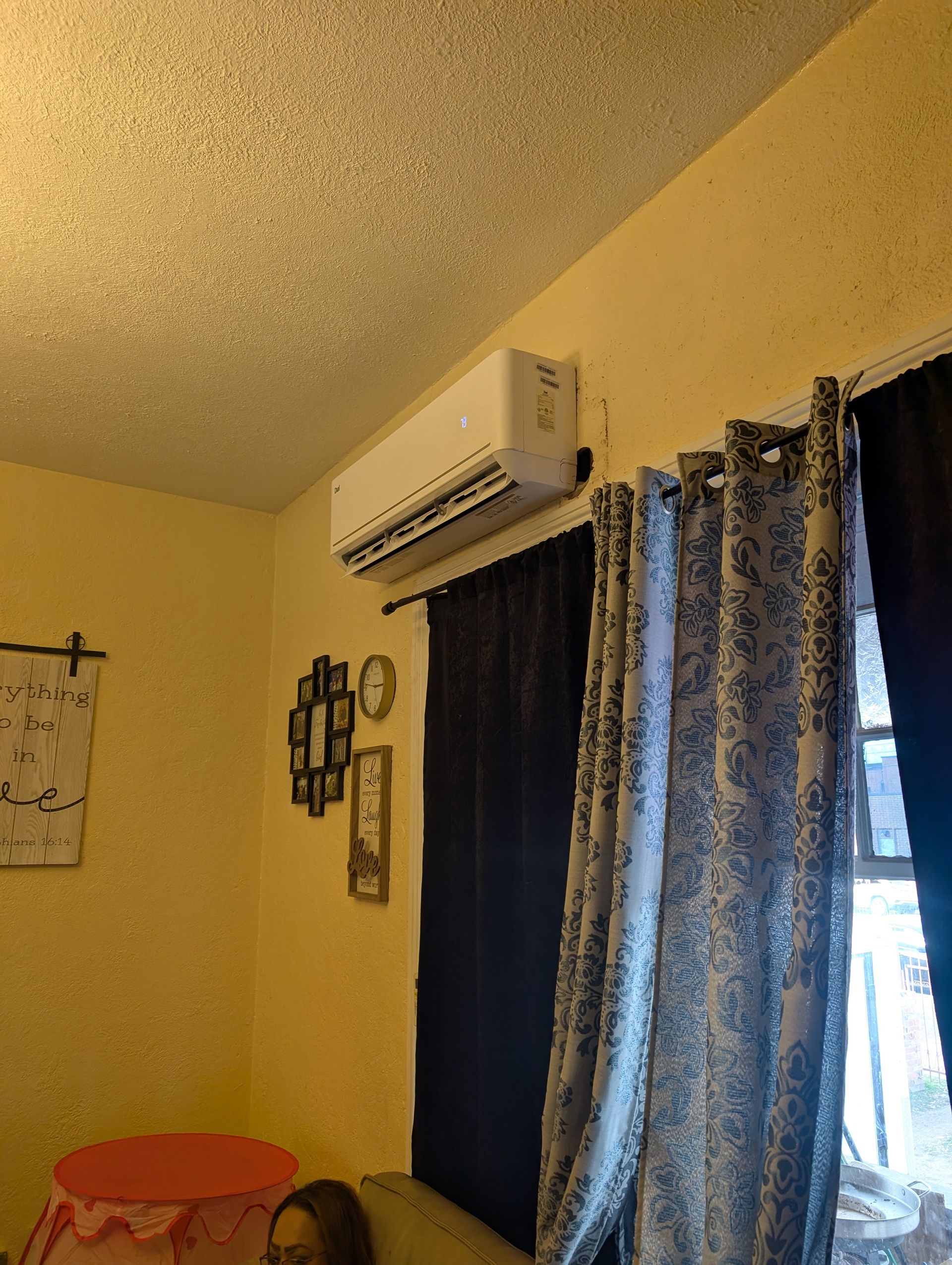 Small room with yellow walls, wall-mounted air conditioner, blue curtains, and a small table.