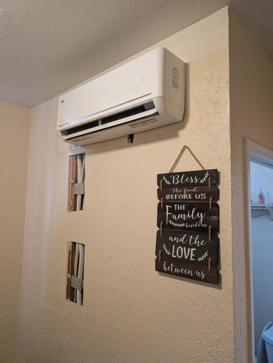 Wall-mounted air conditioner above a hanging chalkboard sign in a beige hallway.