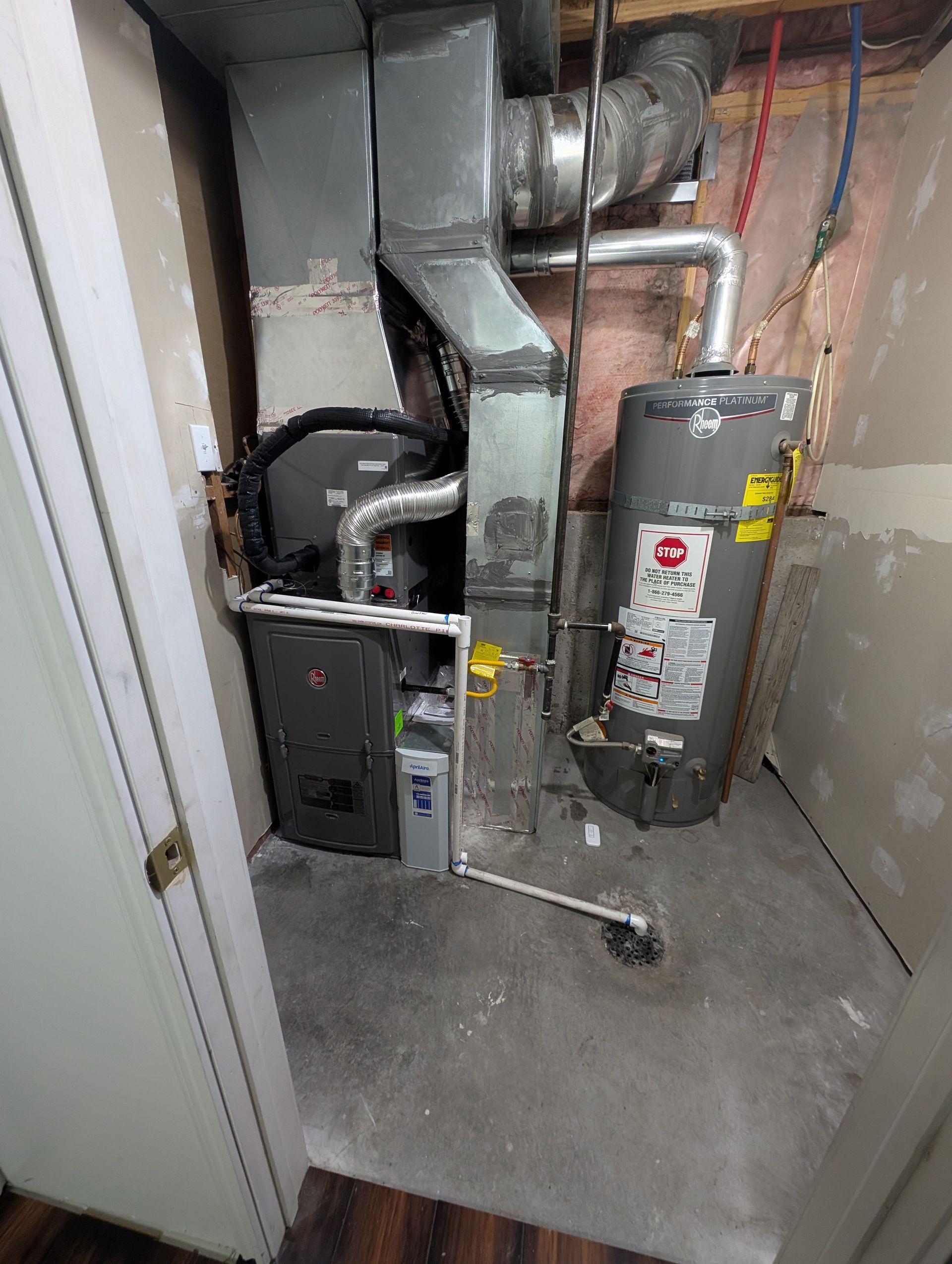 Furnace and water heater in a cramped utility closet with exposed ductwork and pipes