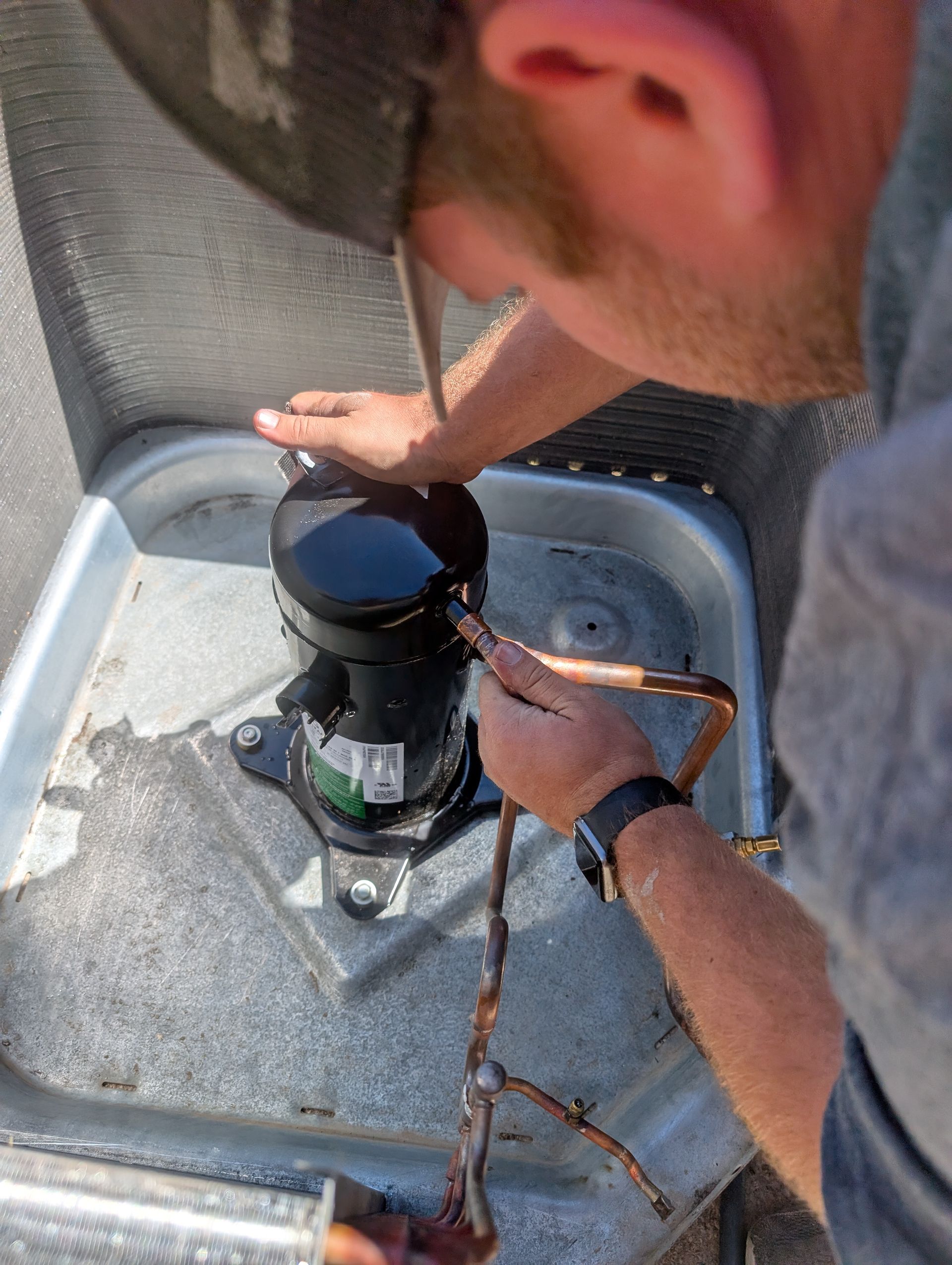 Technician working on a black HVAC compressor unit inside a metal outdoor housing