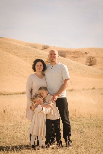 Family of three standing in a golden field with rolling hills in the background.