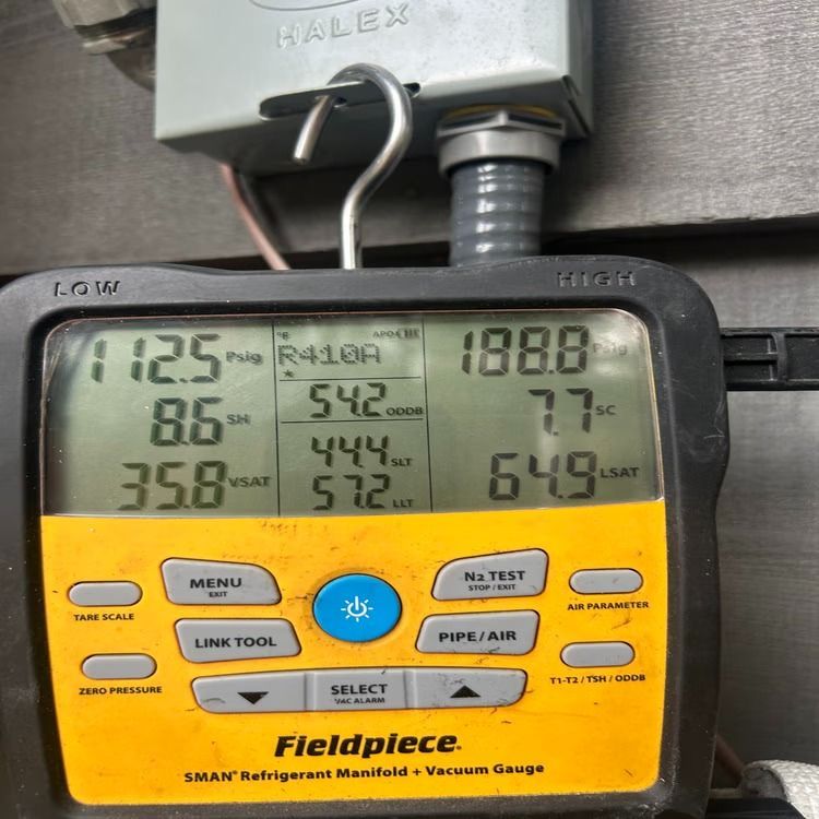 Fieldpiece digital HVAC gauge with yellow buttons displaying pressure and temperature readings attached to copper pipes