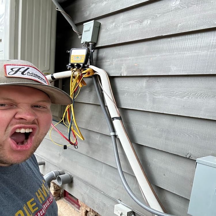 Man posing next to exposed outdoor wiring and a utility meter on a gray house wall