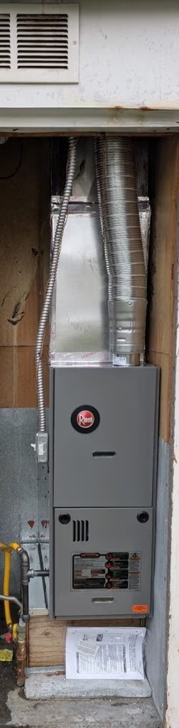 Gray electrical panel and metal ductwork in a narrow utility alcove under a wall vent.