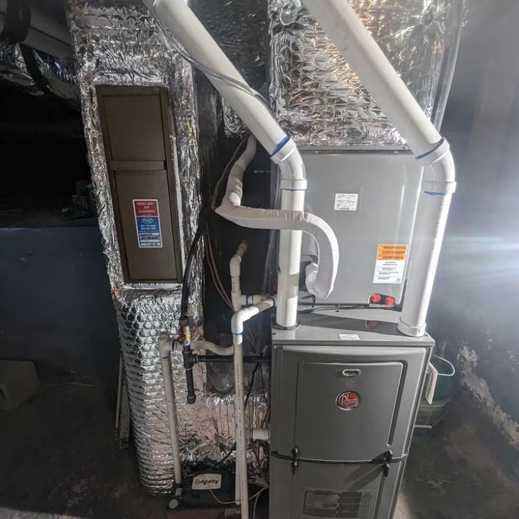 HVAC furnace and air handler in a utility closet with foil-wrapped ductwork and white PVC vent pipes
