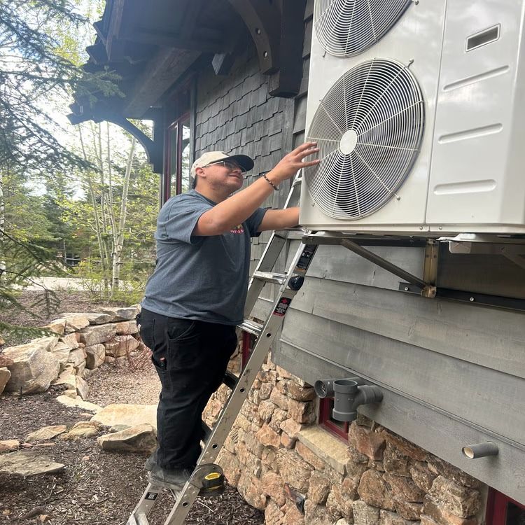 Technician inspecting an outdoor HVAC unit mounted on a house wall.