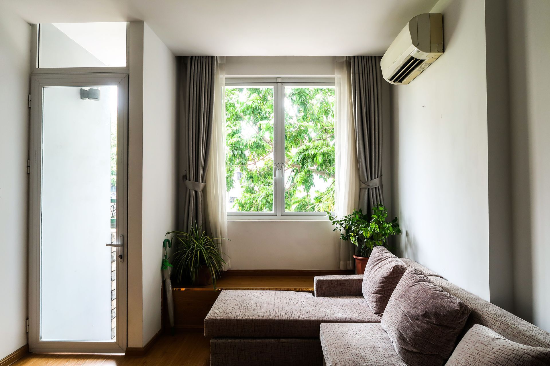 Small bright living room with sofa, window plants, and an air conditioner