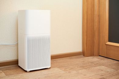 White air purifier on a wooden floor beside a wall and doorway.
