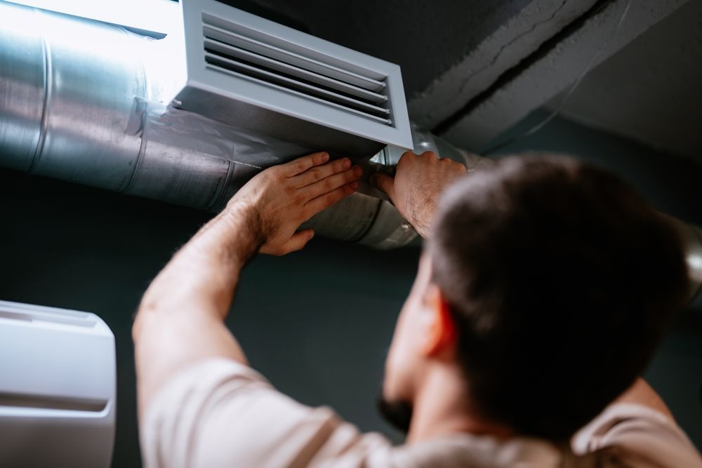 Person reaching up to adjust a ceiling air vent in a dimly lit room
