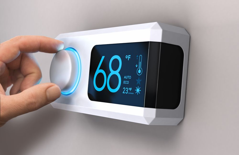 Hand turning a round knob on a wall thermostat showing 68° on a blue digital display