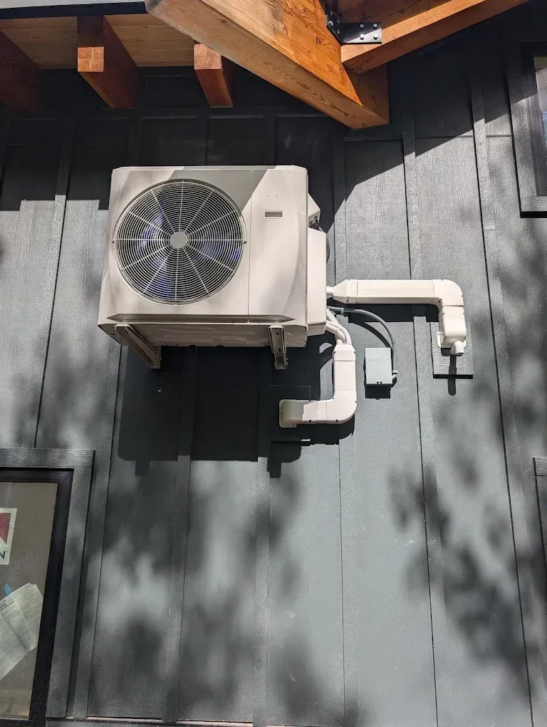 Outdoor air-conditioning unit mounted on a gray wall beneath wooden eaves