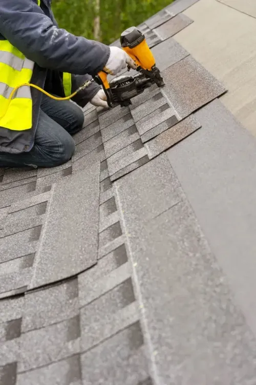 Roofing company installing shingles with a nail gun on a sloped roof in Aurora, IL.