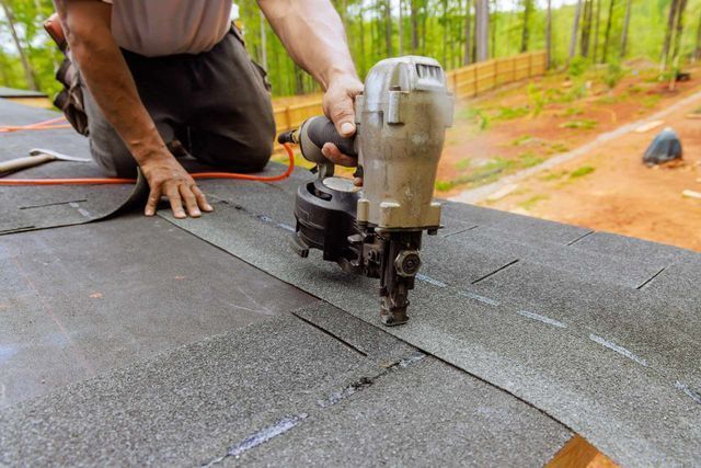 A worker uses a pneumatic nail gun for asphalt shingle roof installation in Aurora, IL.