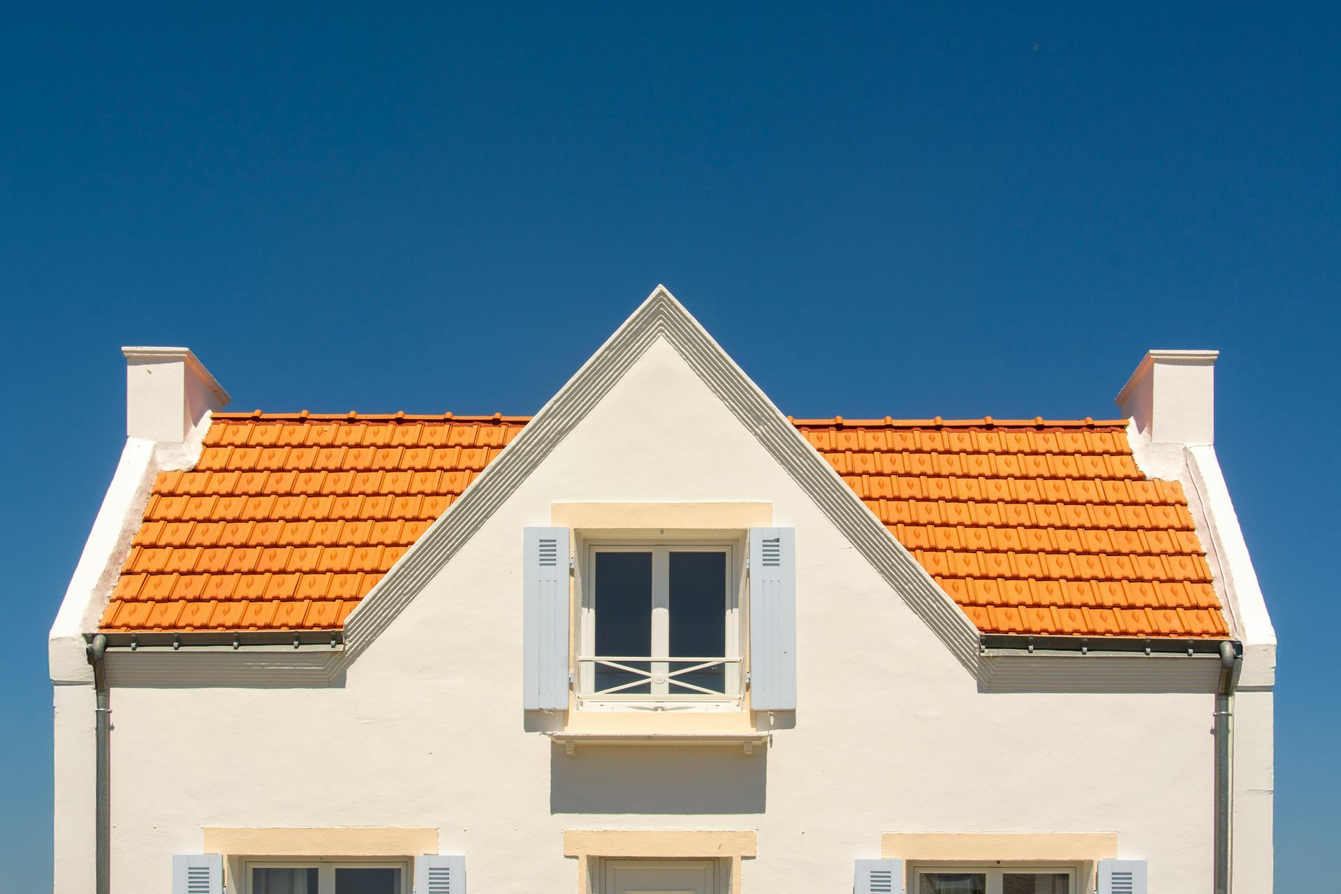 A person uses a teal cordless drill to fasten a piece of orange metal roofing near a white gutter on a construction site.