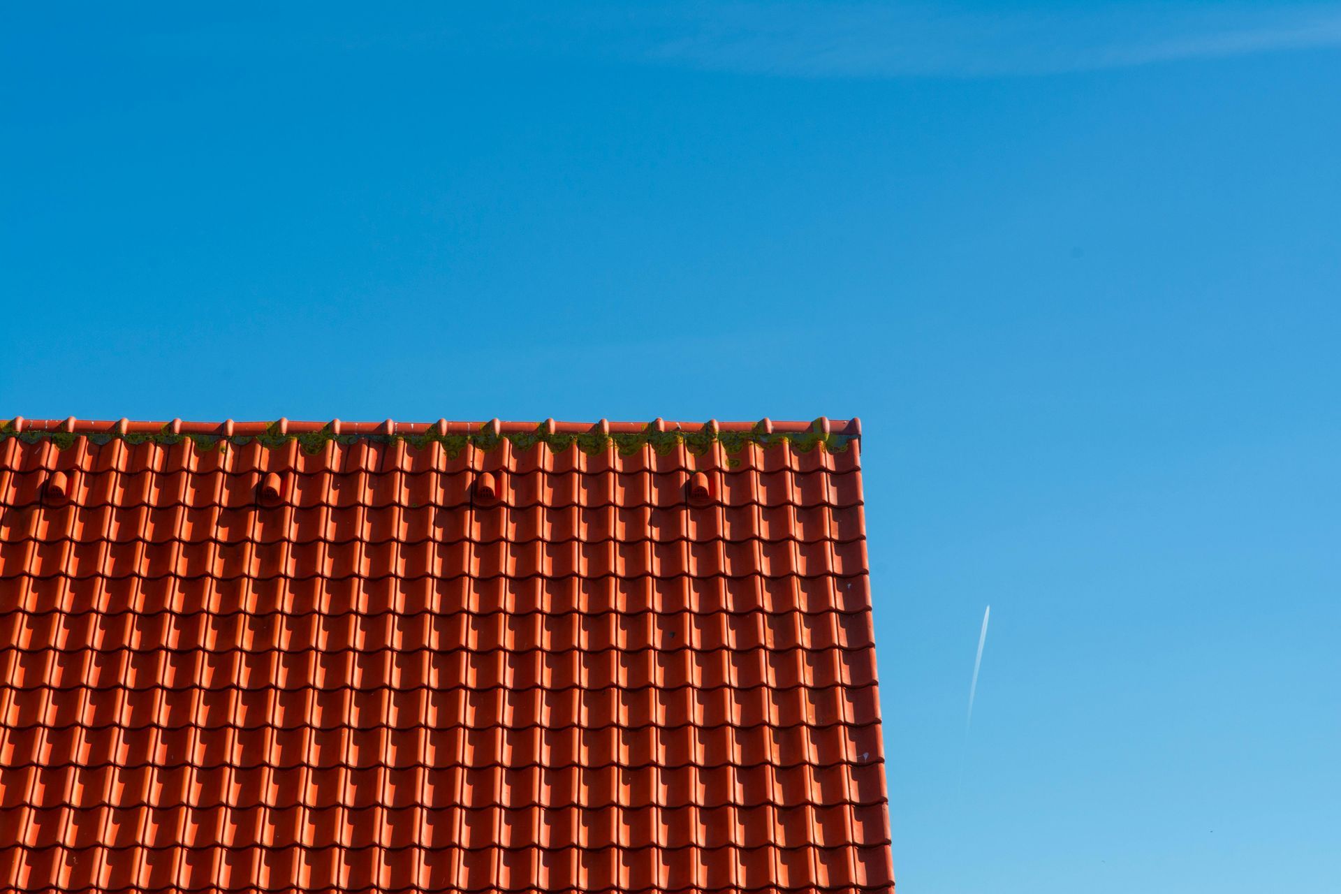 Two construction workers wearing safety vests and hard hats install solar panels on a tiled residential roof.