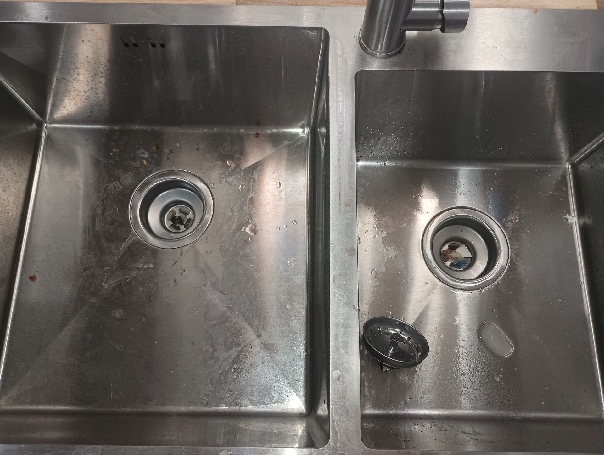 Stainless steel double kitchen sink with faucets and a few dishes in the right basin