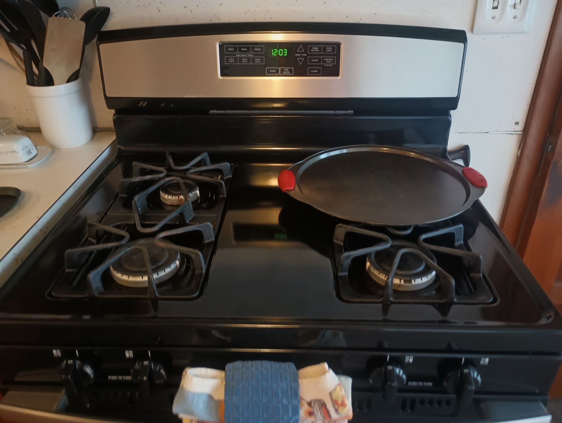 Black gas stove with a frying pan and a red spoon on the front burners in a kitchen