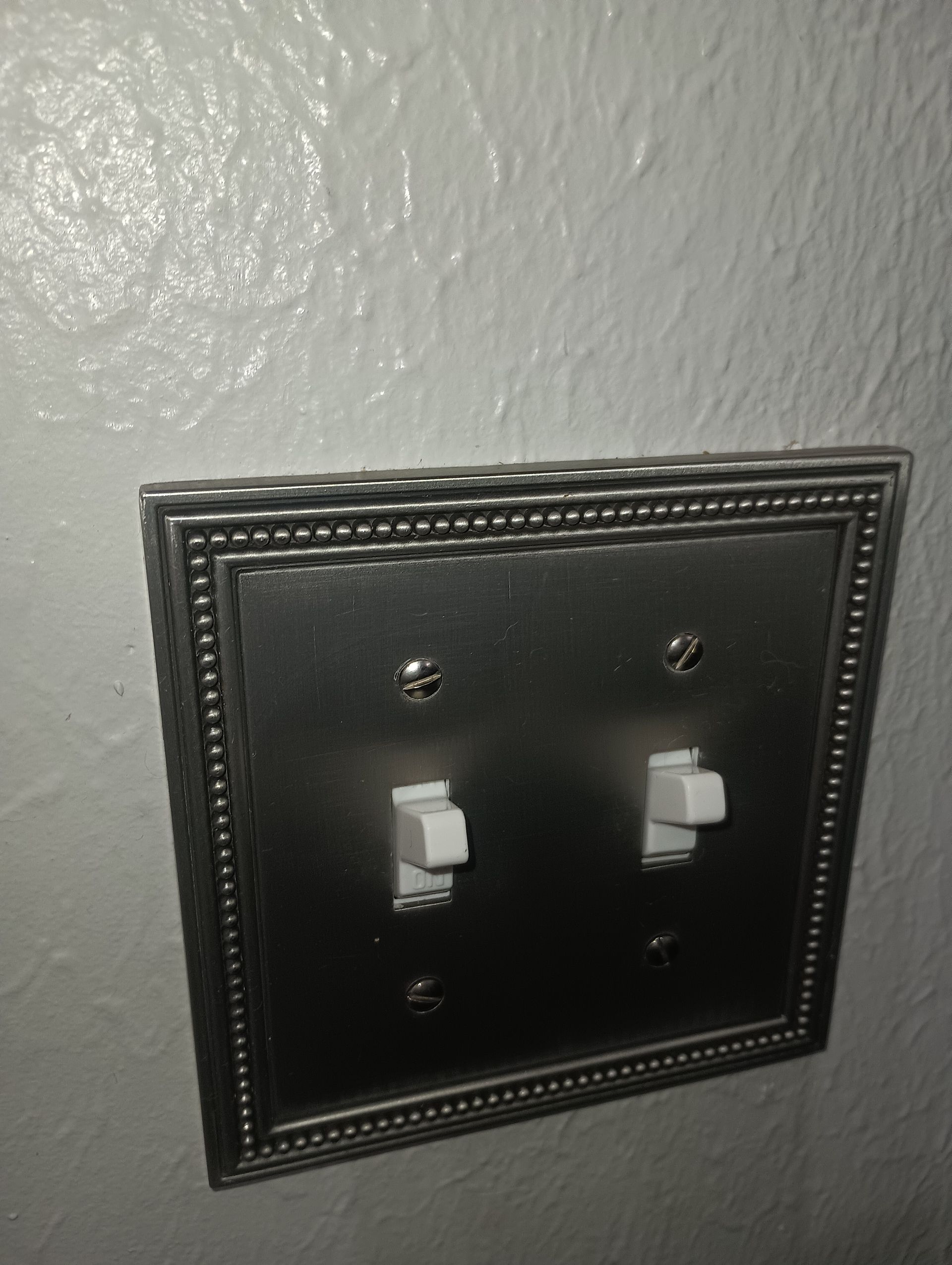 Black decorative double light switch plate on a textured wall.