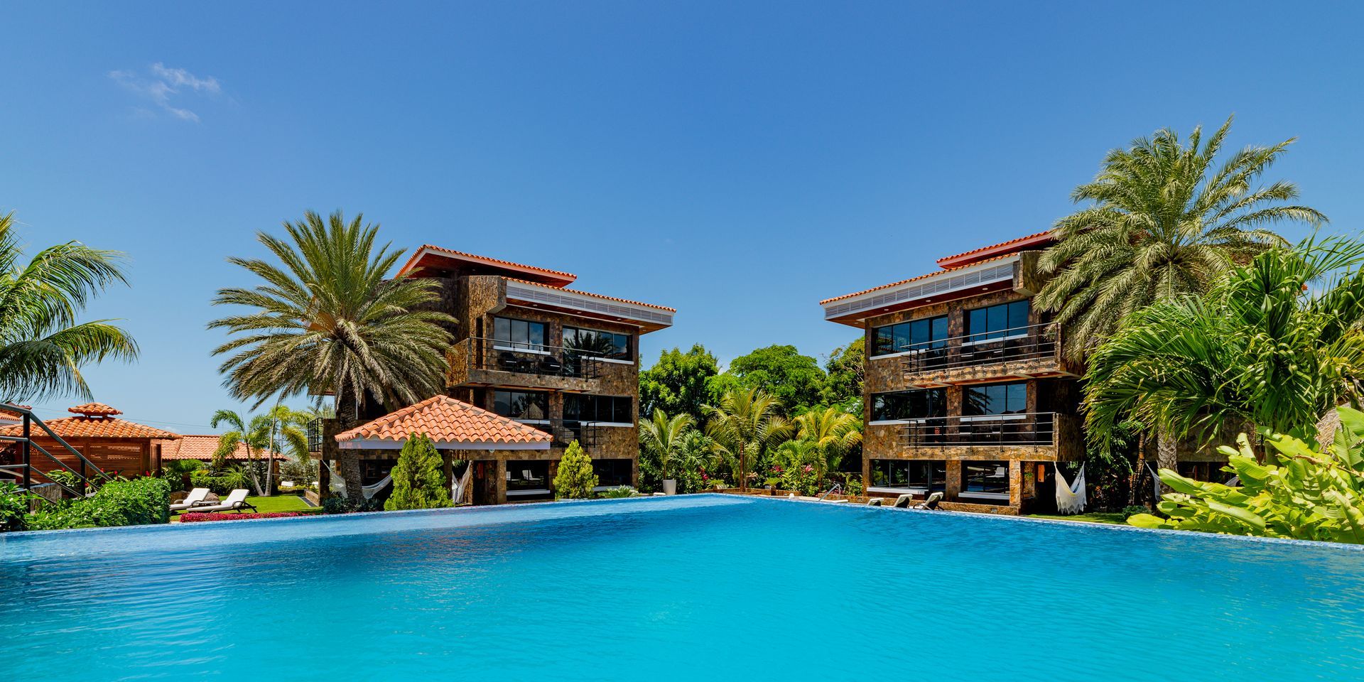 Resort pool with turquoise water, palm trees, and tropical villas under a clear blue sky