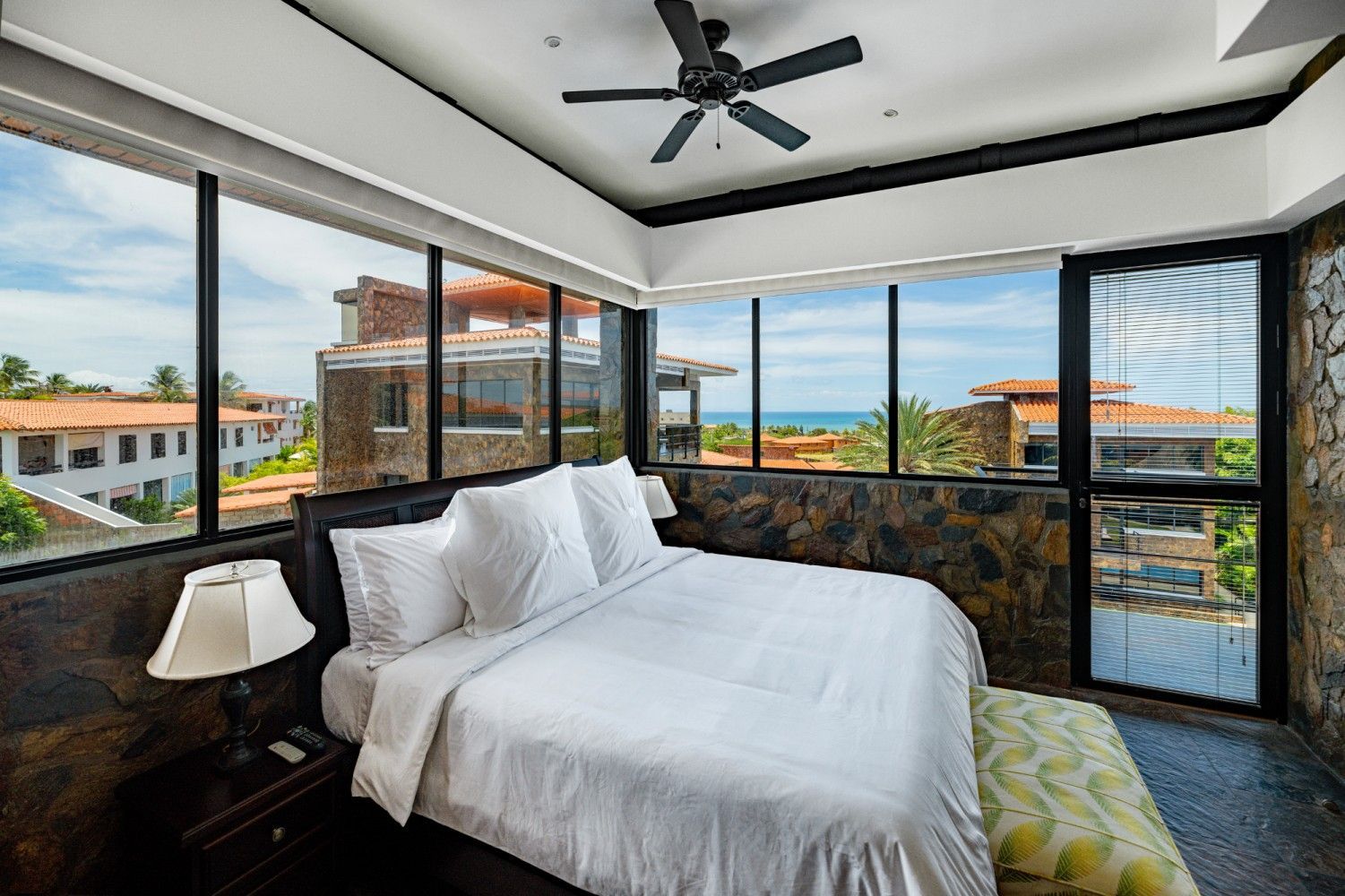 Modern bedroom with large windows, king bed, and ocean view behind black-framed glass walls