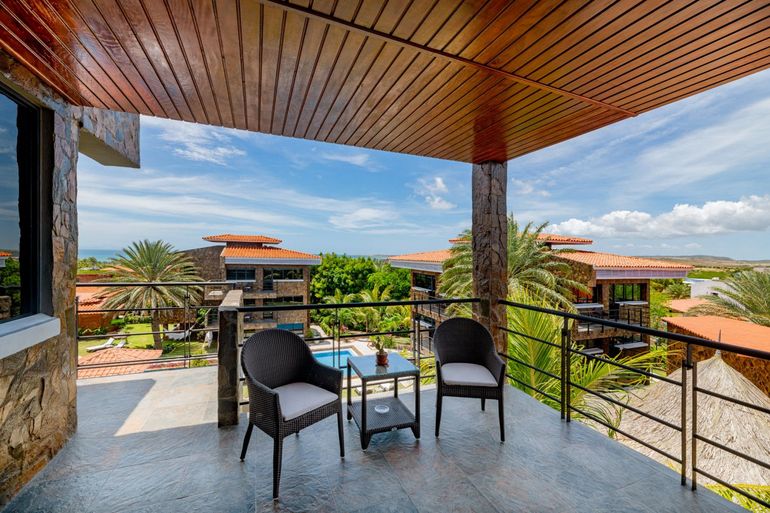 Covered patio with two chairs and a table overlooking a tropical neighborhood and blue sky