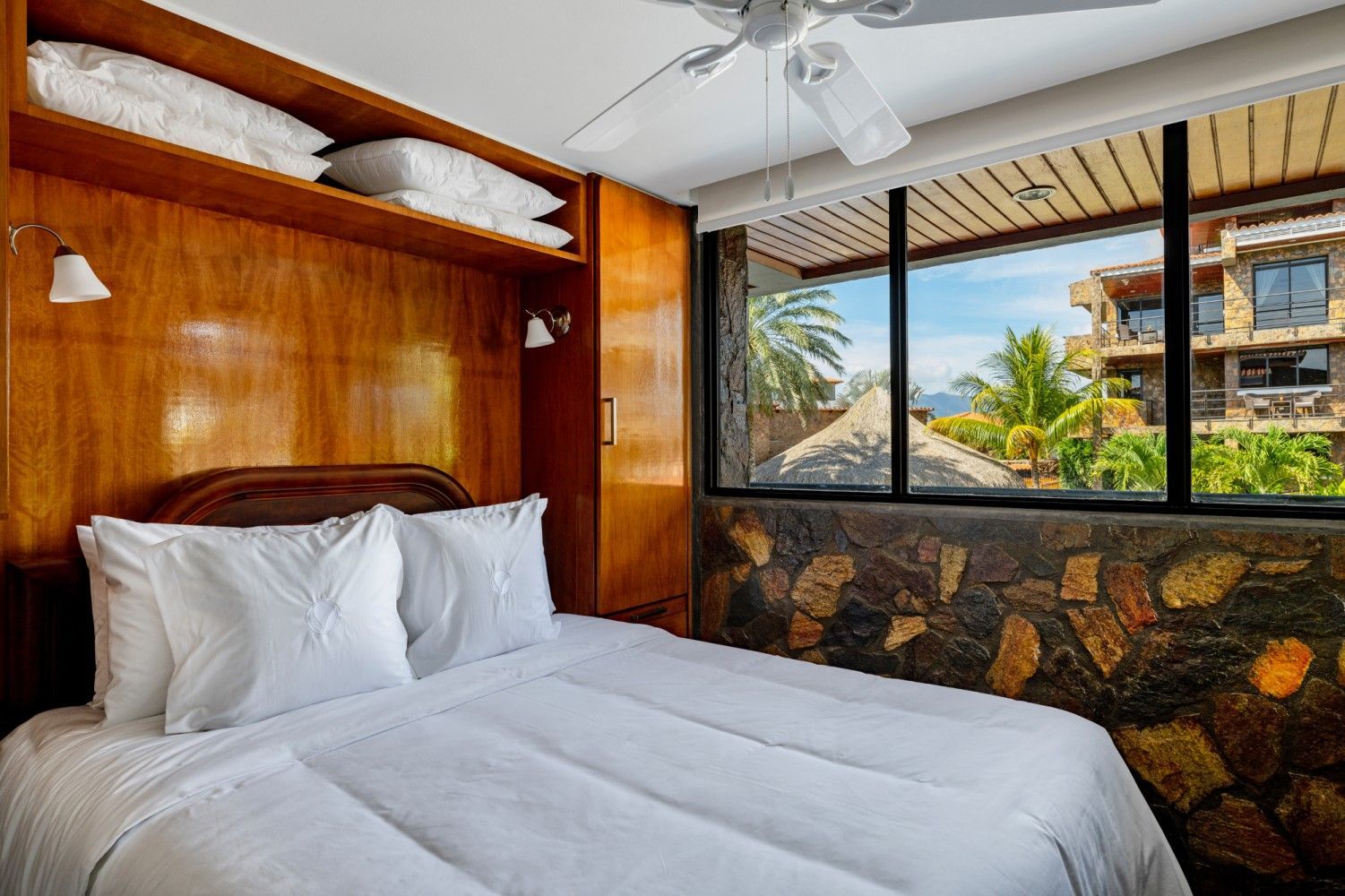 Cozy bedroom with white bed, wooden walls, stone window ledge, and ocean view outside
