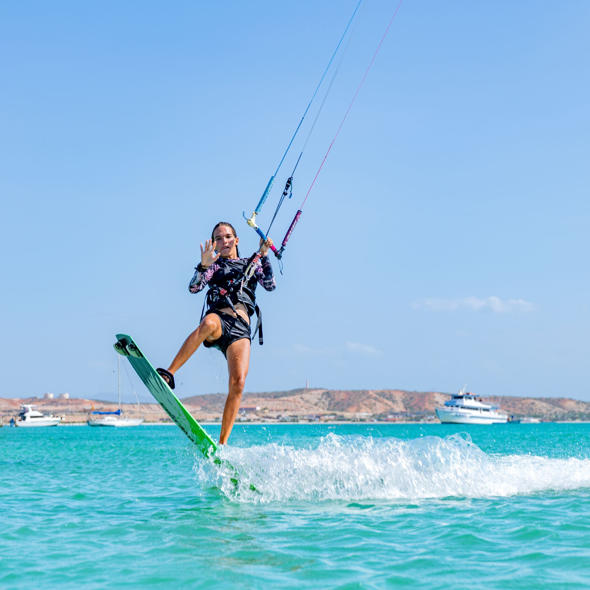 Kitesurfer gliding over turquoise water near the shore, with a boat and coastline in the background