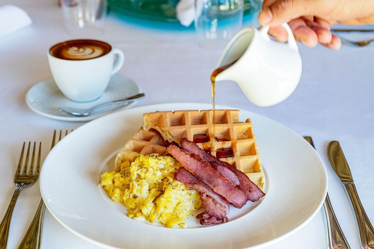 Breakfast plate with waffles, scrambled eggs, bacon, and coffee on a white table