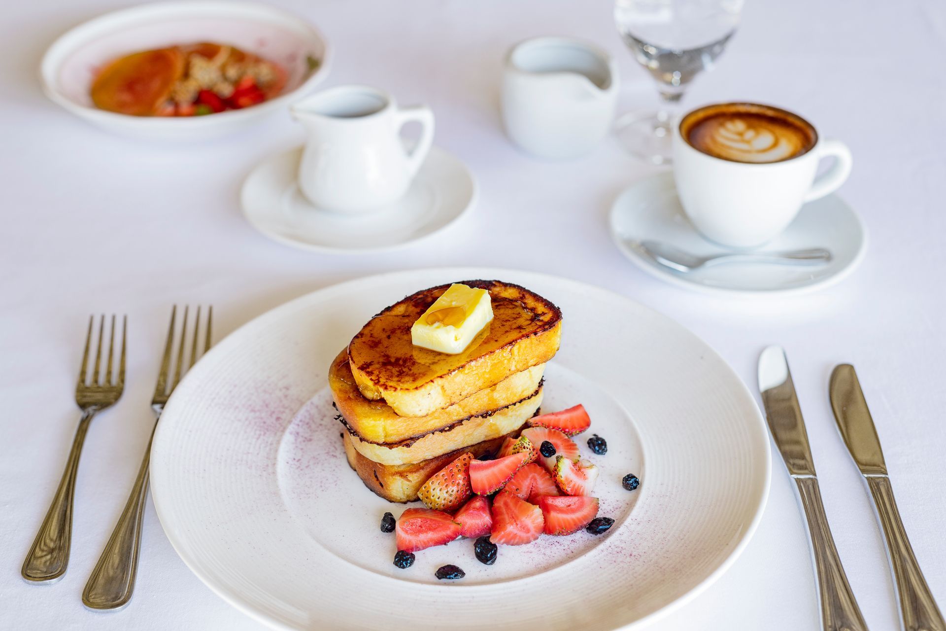 Breakfast plate with French toast, berries, coffee, and white tableware on a bright table
