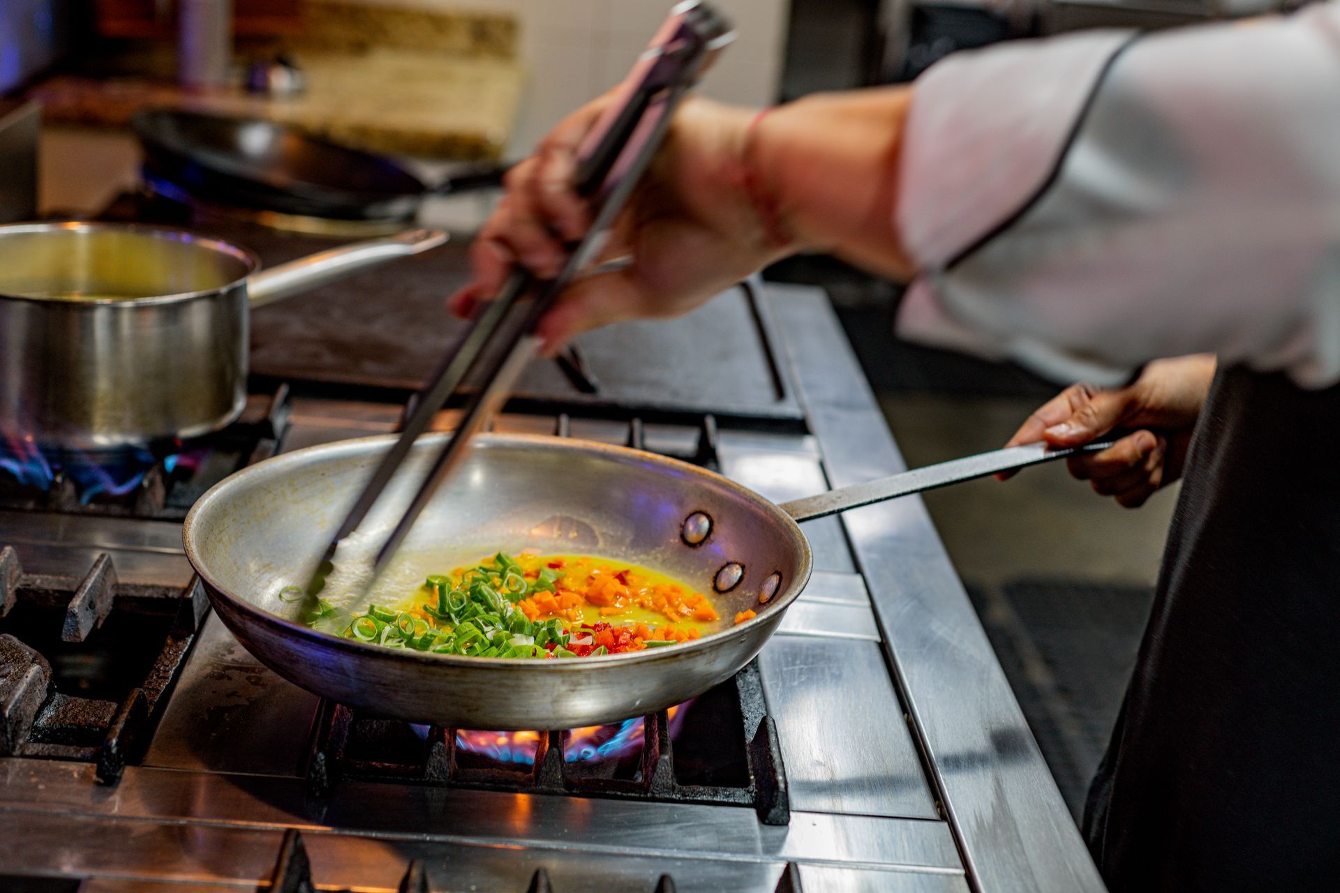 Chef stirring colorful vegetables in a pan on a gas stovetop