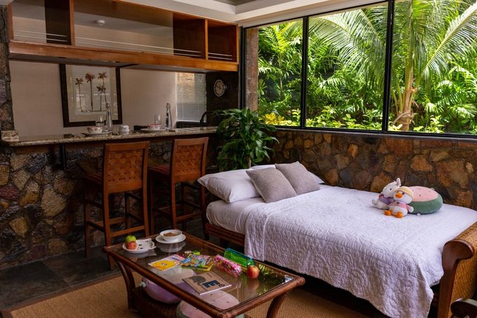 Tropical open-air bedroom with a bed, breakfast tray, and large windows overlooking lush greenery