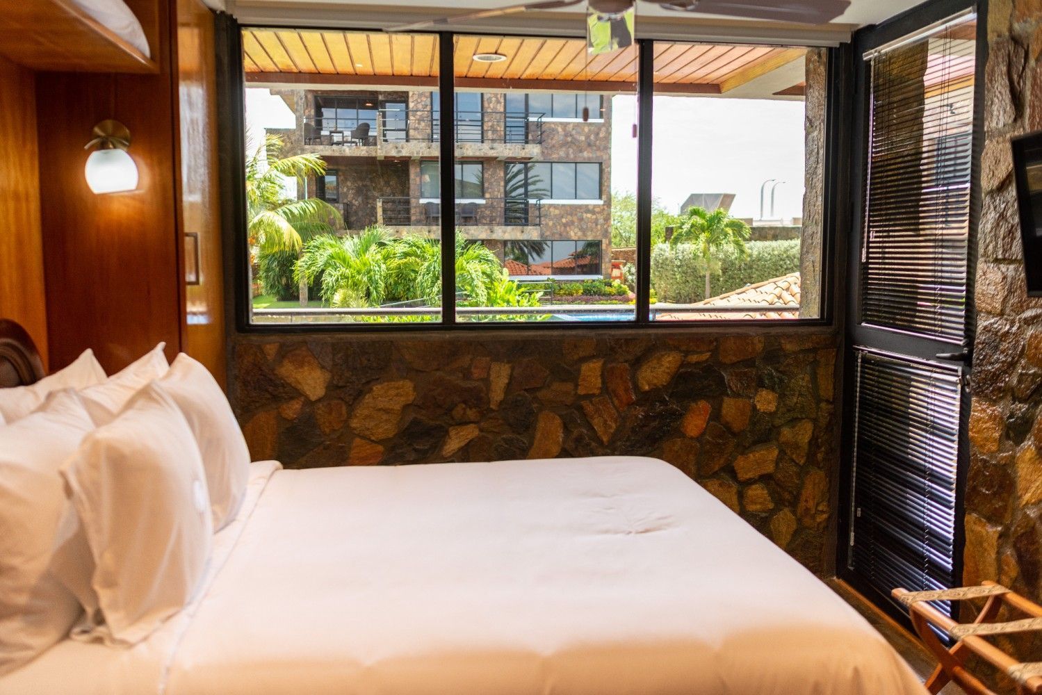 Cozy hotel room with a white bed, wood paneling, and a large window overlooking a patio and courtyard