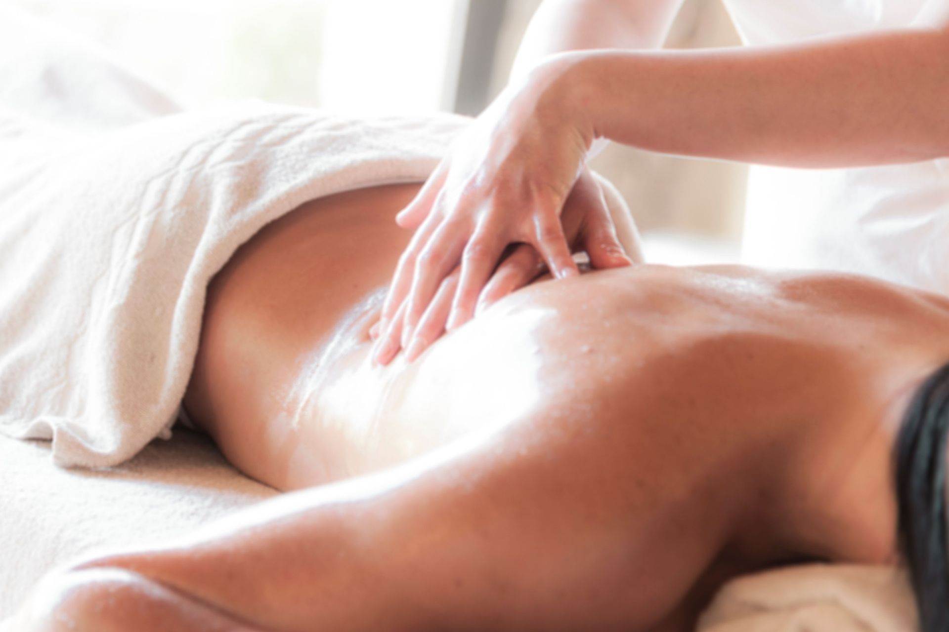 Person receiving a back massage on a spa table, covered with a white towel