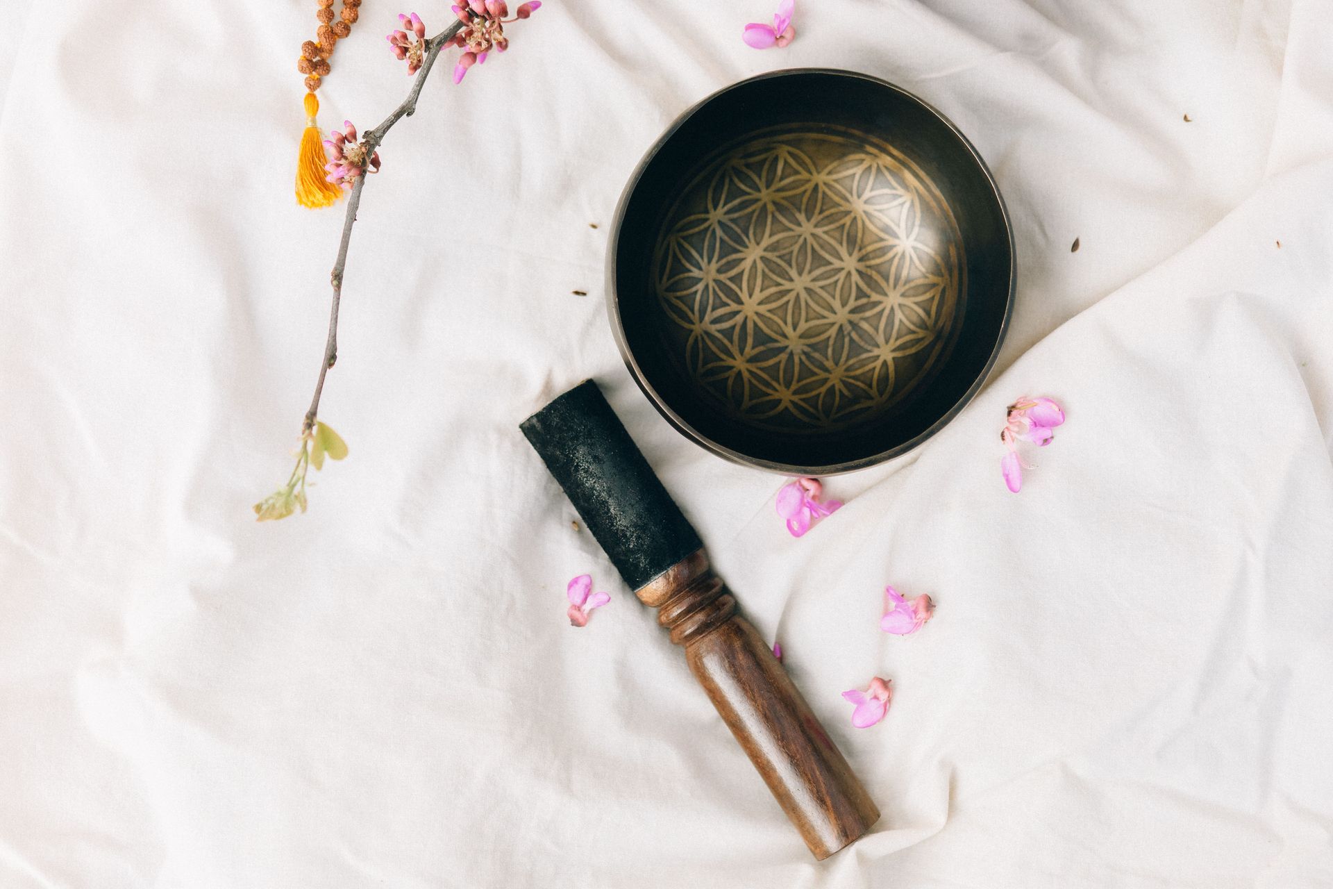 Black singing bowl, brush, and pink petals on a white cloth