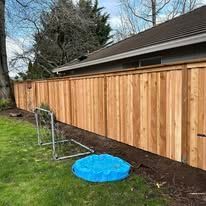 A wooden fence runs along the back of a house, next to a grassy yard with a small blue plastic pool and a soccer goal.