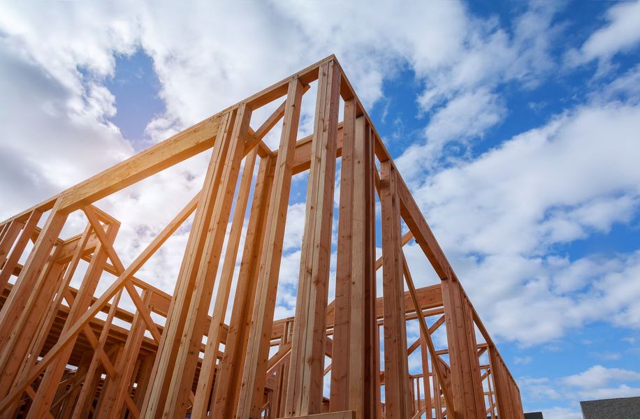Wooden framing of an unfinished building against a blue, partly cloudy sky.