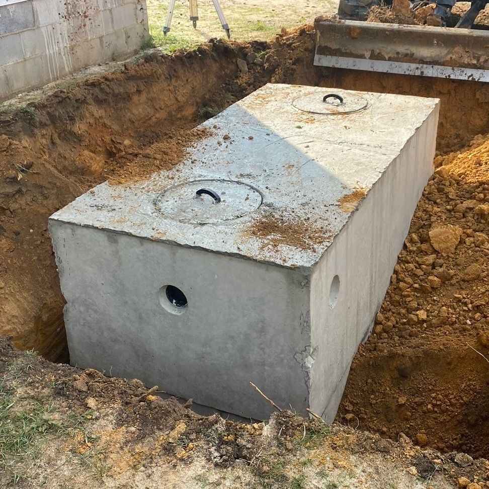 Black corrugated pipe junction set in a dirt trench, secured with straps and surrounded by stakes.