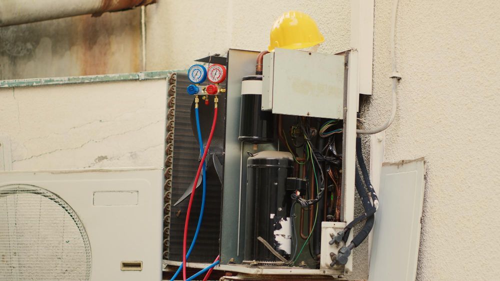 HVAC unit being serviced outdoors, with gauges attached. A yellow hard hat rests on top.