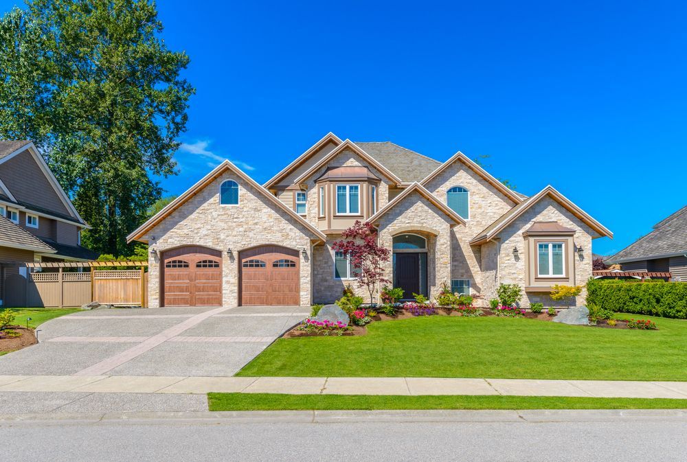 Two-story brick house with a three-car garage, manicured lawn, and blue sky.