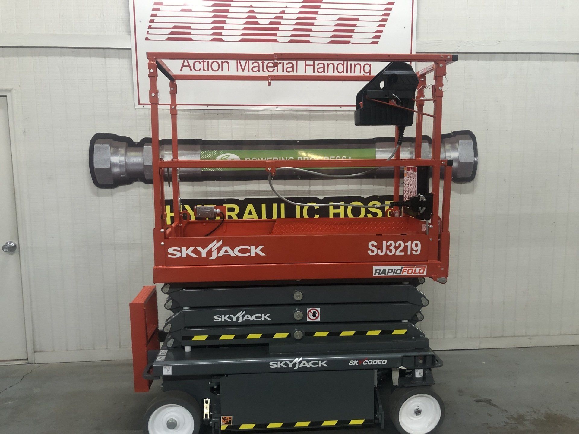 Red Skyjack scissor lift parked indoors beneath a large hose reel fixture
