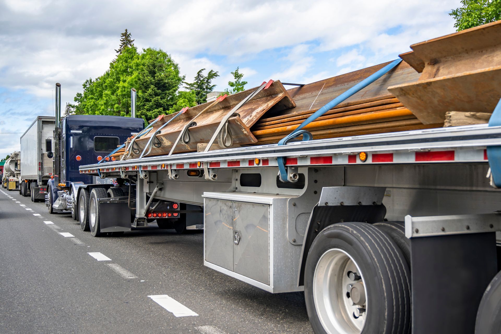 Flatbed truck hauling wood debris on a highway, with traffic behind and cloudy skies.