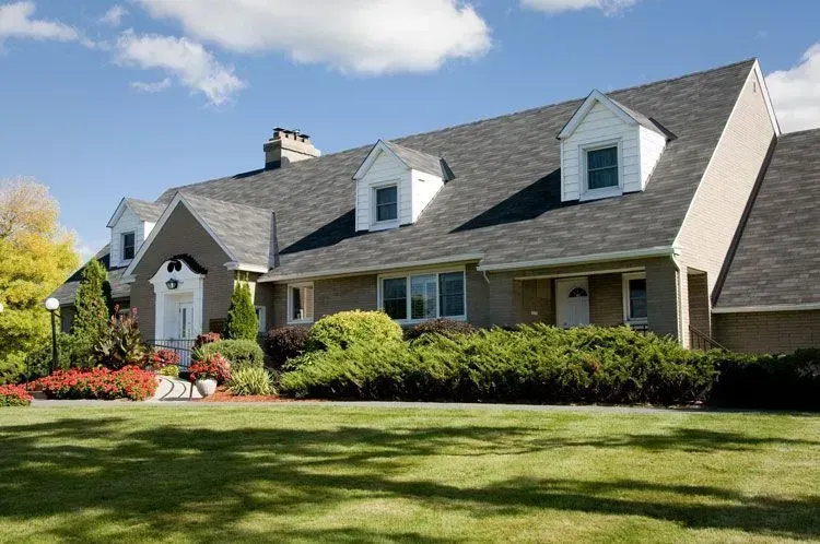 Suburban house with gray roof, front porch, and manicured lawn under a clear blue sky