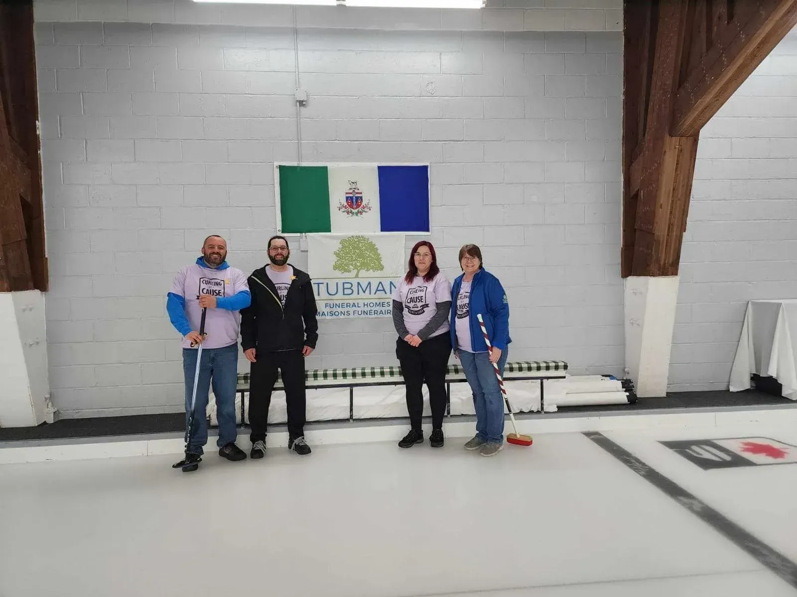 Five people posing in an indoor sports hall beside a curling target and event banner