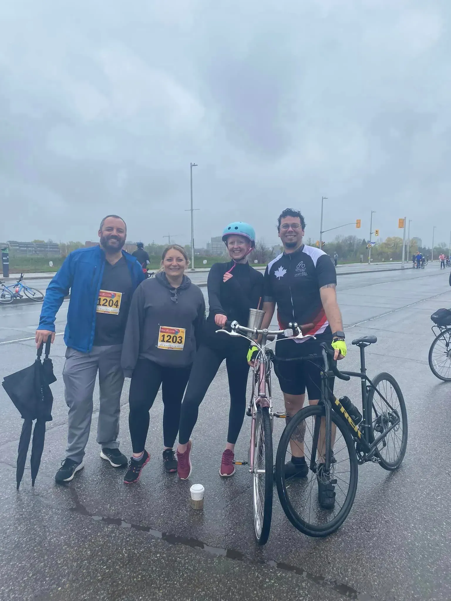 Four cyclists posing with bikes on a wet road under a gray, cloudy sky