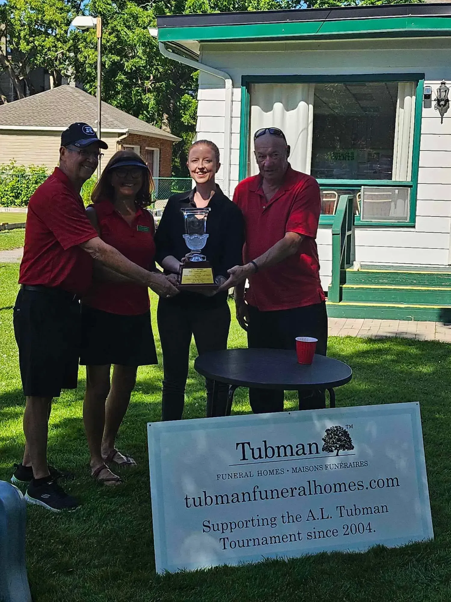 Four people posing with a trophy beside a sign at an outdoor event