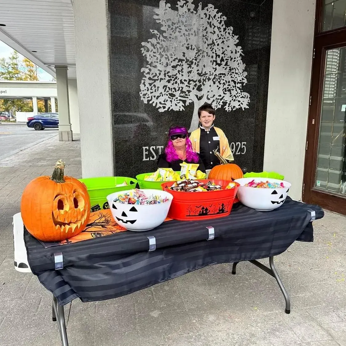 Halloween display with carved pumpkin, candy bowls, and two children behind a table outdoors